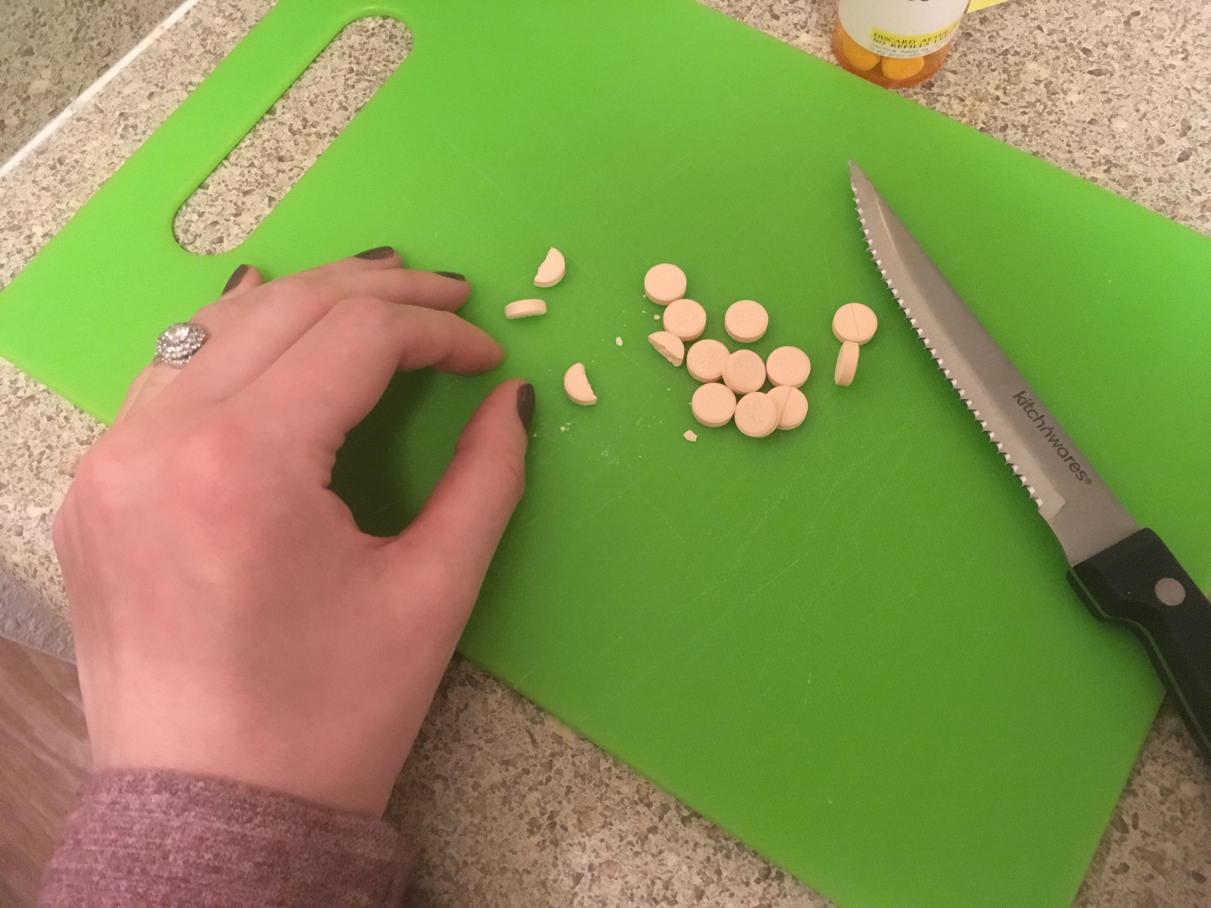 Jenna cutting pink prednisone tablets on green cutting board to get the right dose