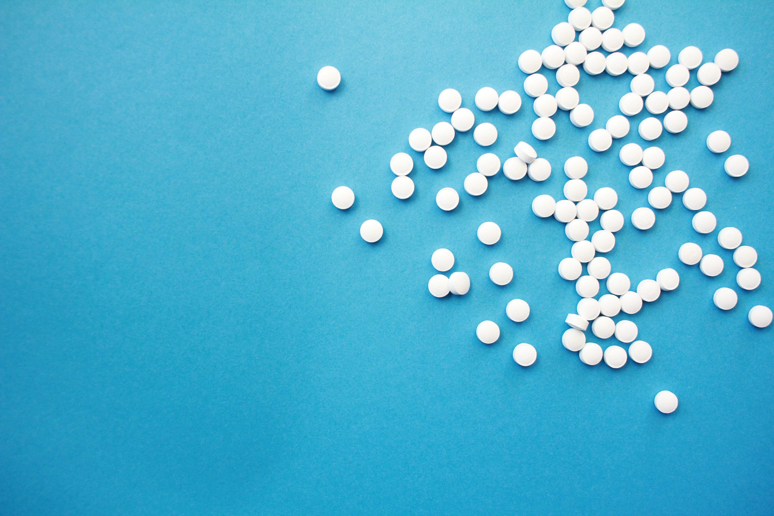 Dozens of white pills spilling onto blue surface