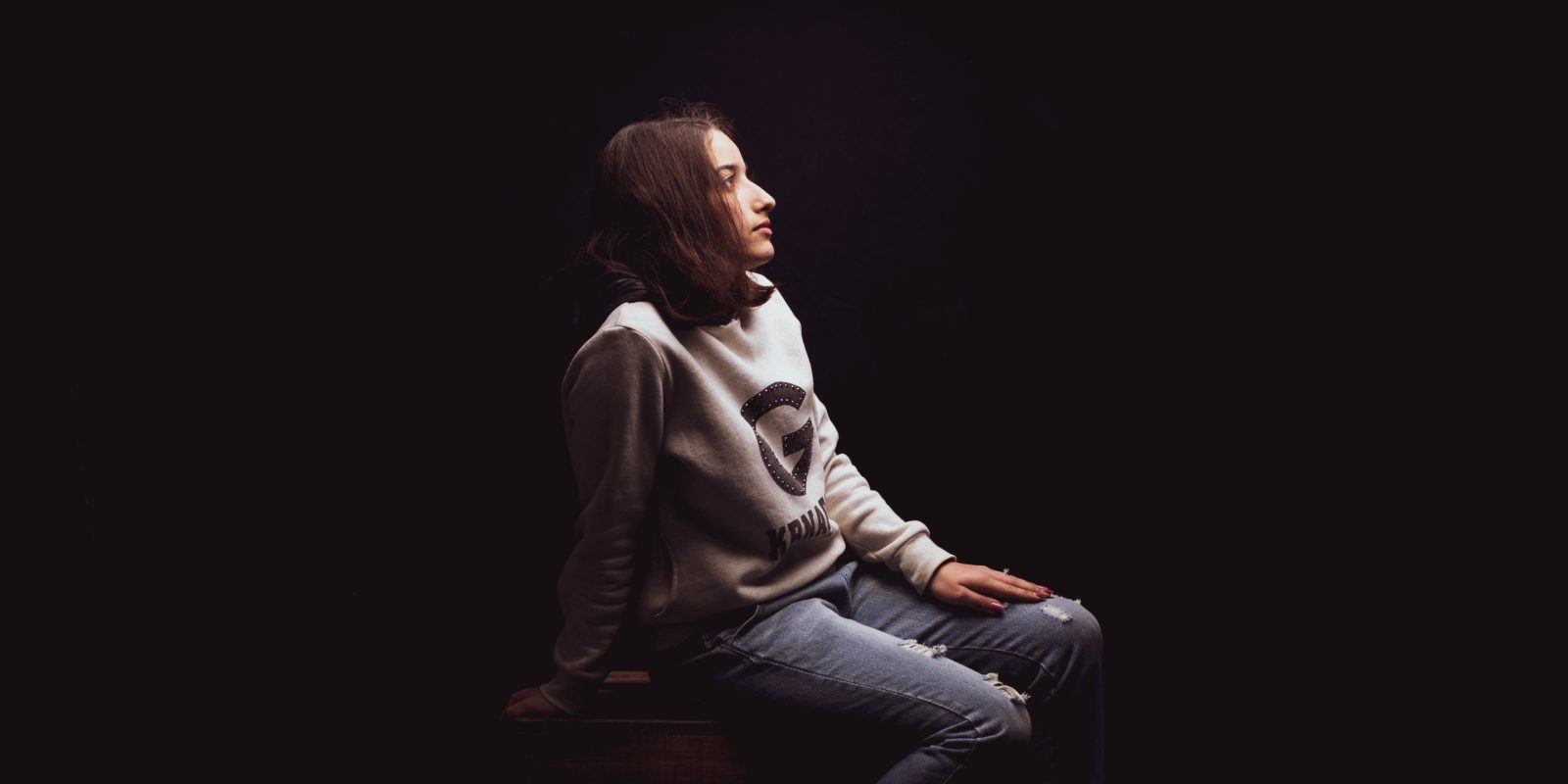 Woman sitting on a stool in the darkness with a studio light on her face