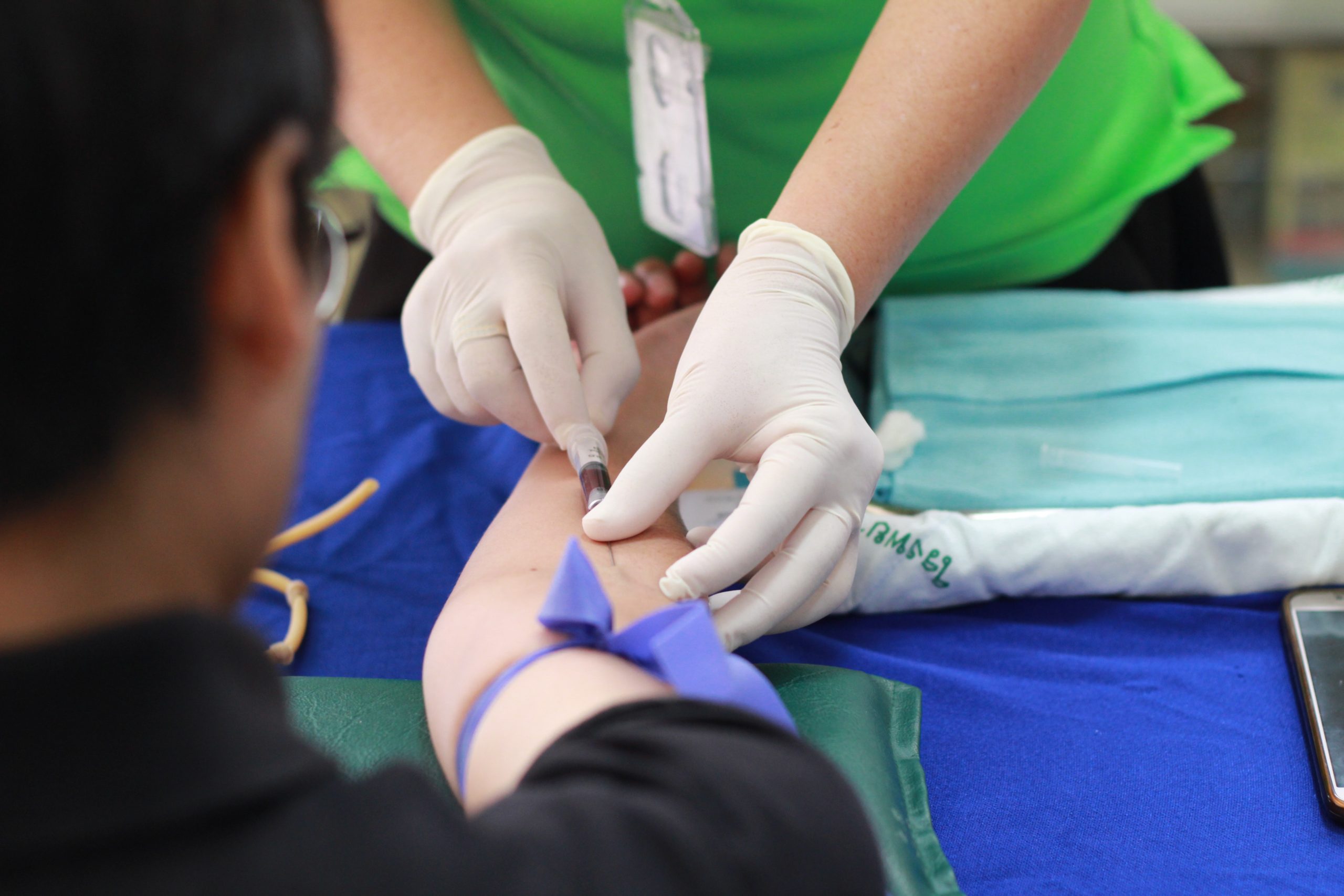 Phlebotomist with white gloves inserting needle in man's arm for blood work