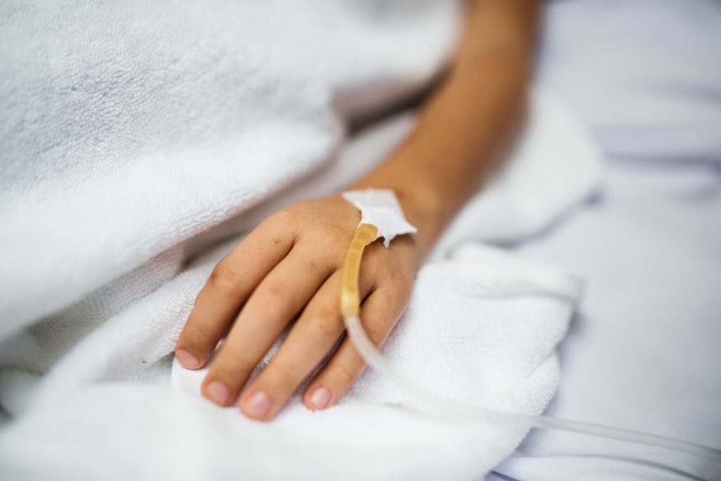 Closeup of woman's hand resting on blue hospital bed with IV in the back of her hand