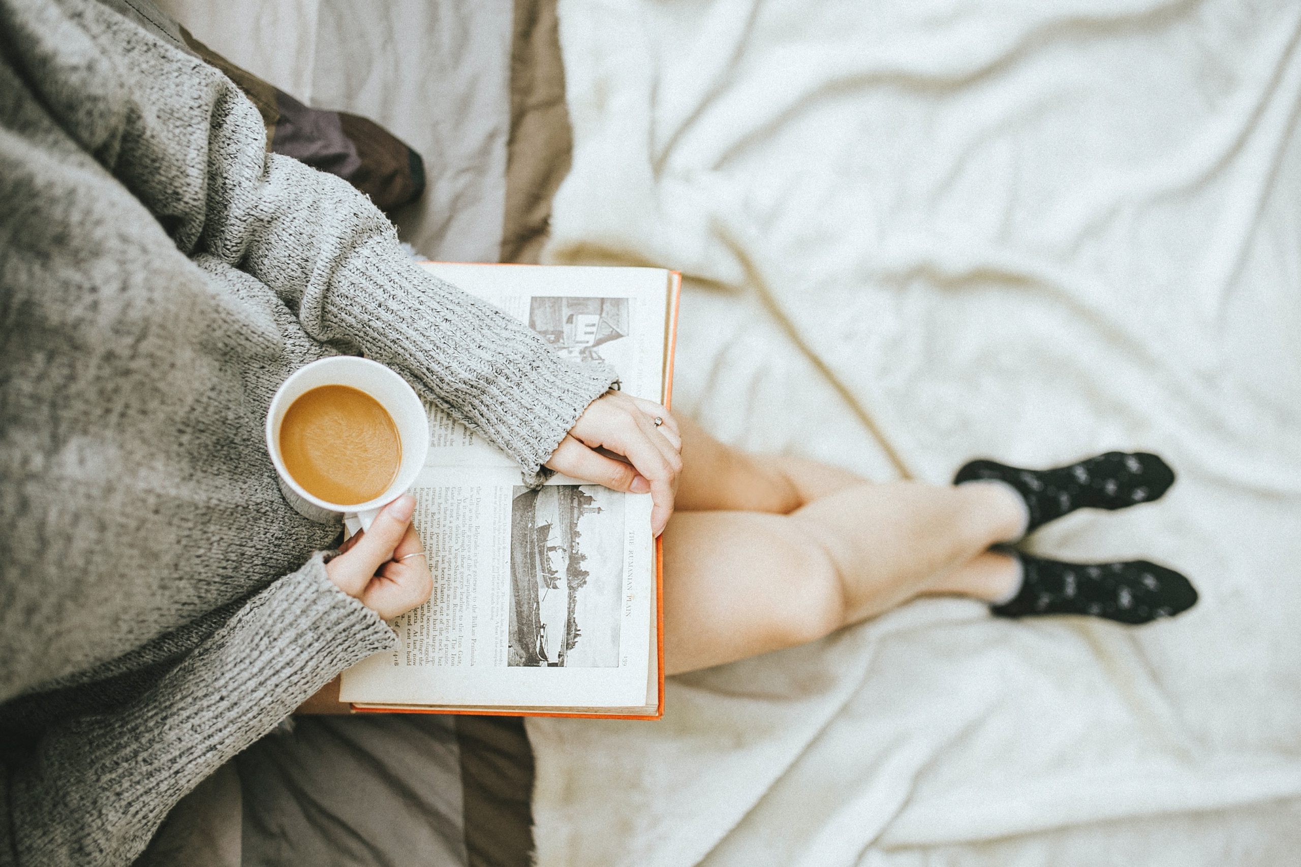 Woman reading book on lap and holding coffee mug