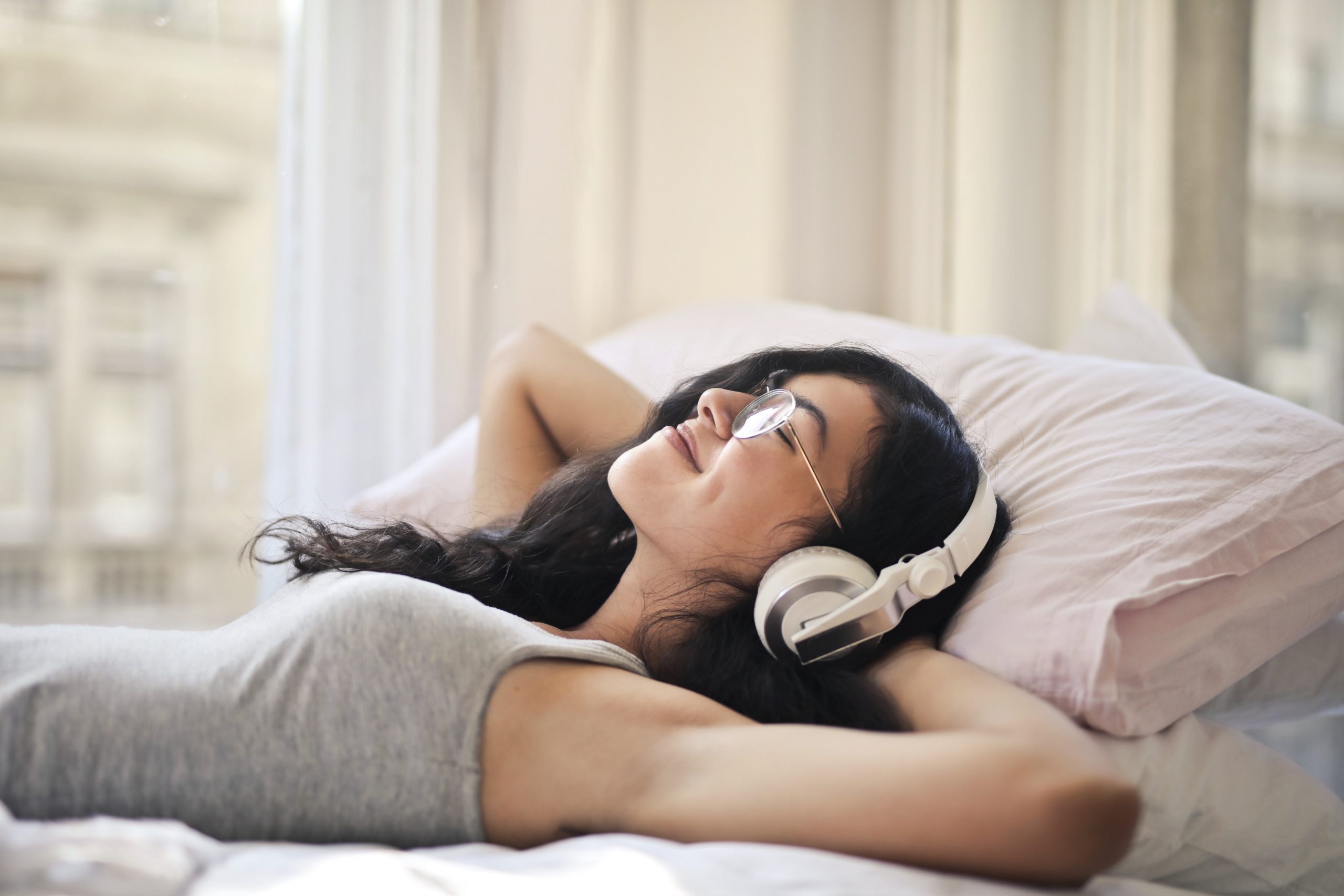 Girl laying on her back in bed wearing headphones and relaxing