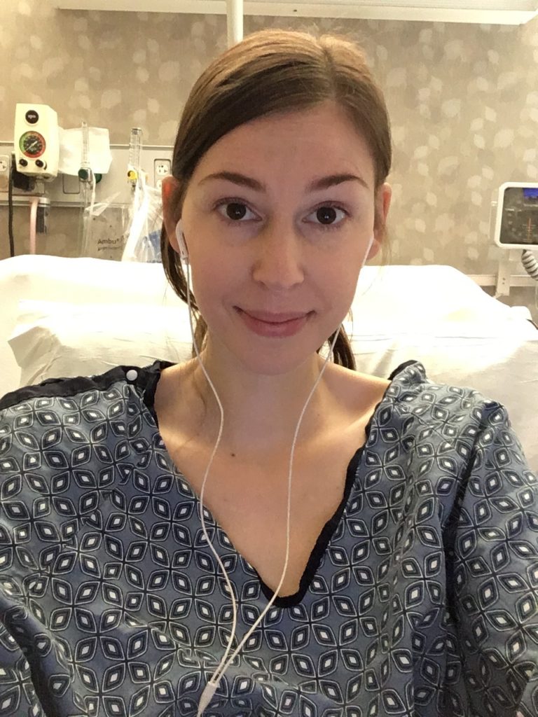 Jenna wearing blue hospital gown and headphones smiling tiredly