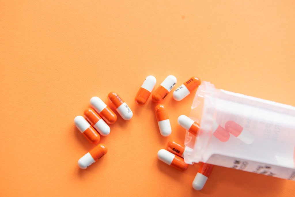 Orange and white pills spilling out of medication bottle onto orange table.