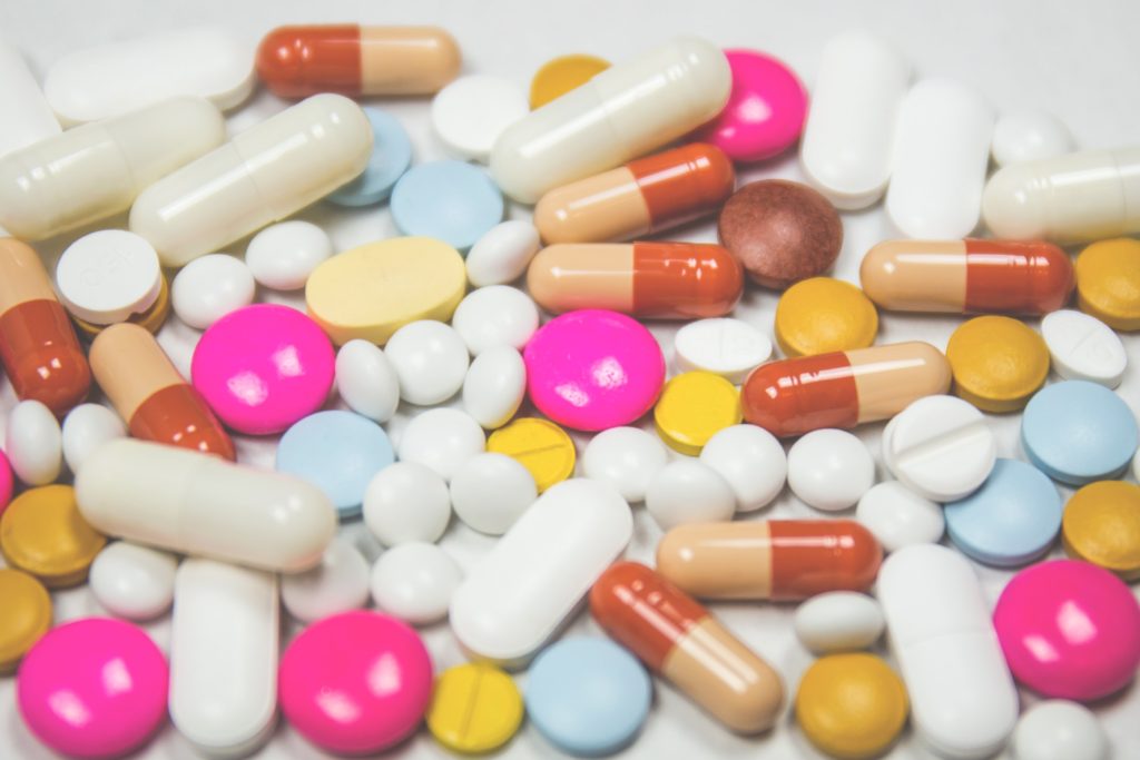 Pile of pink, blue, white, orange, and yellow pills on white table