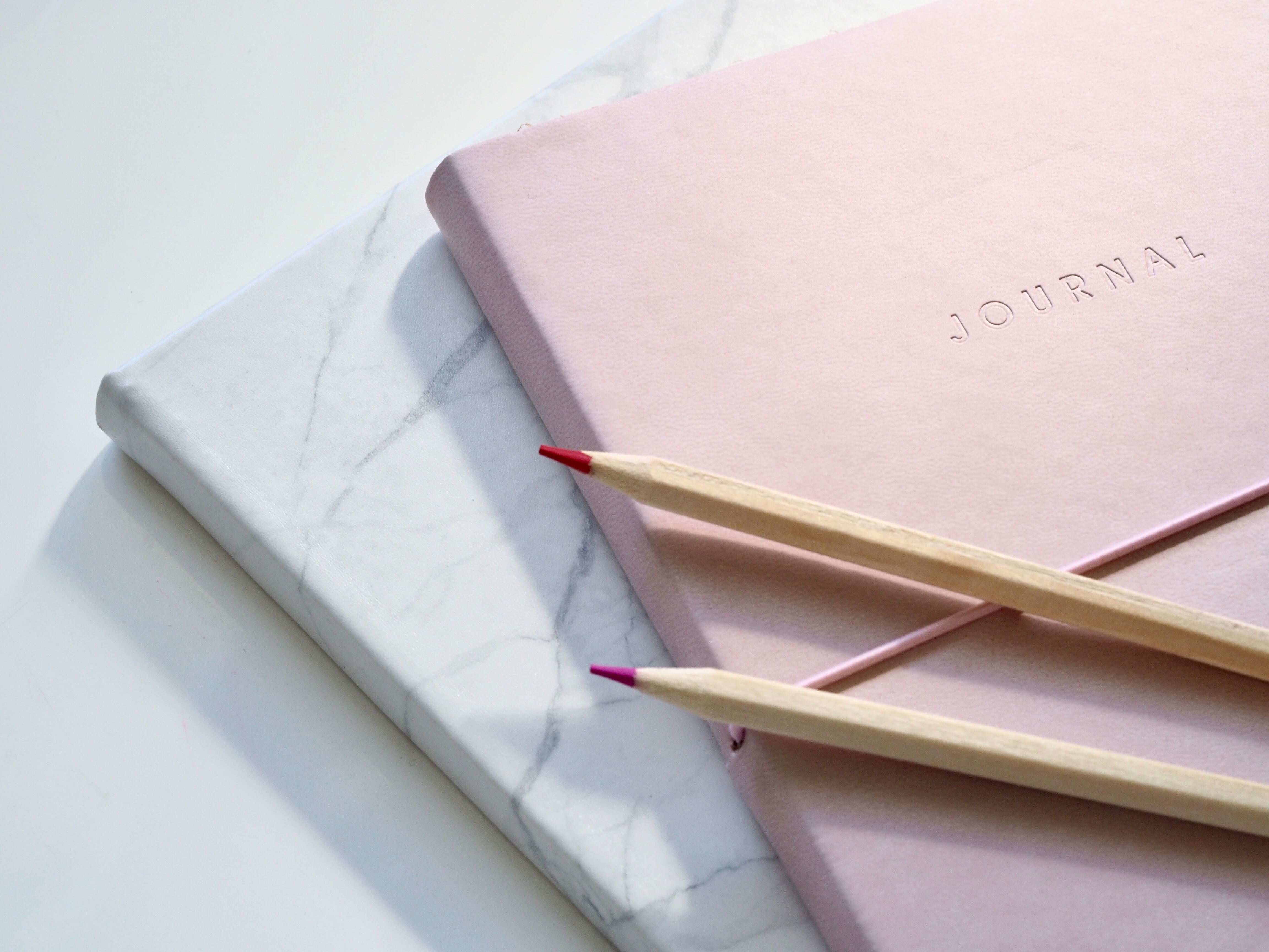 Two colored pencils sitting on pink and white marble notebooks.