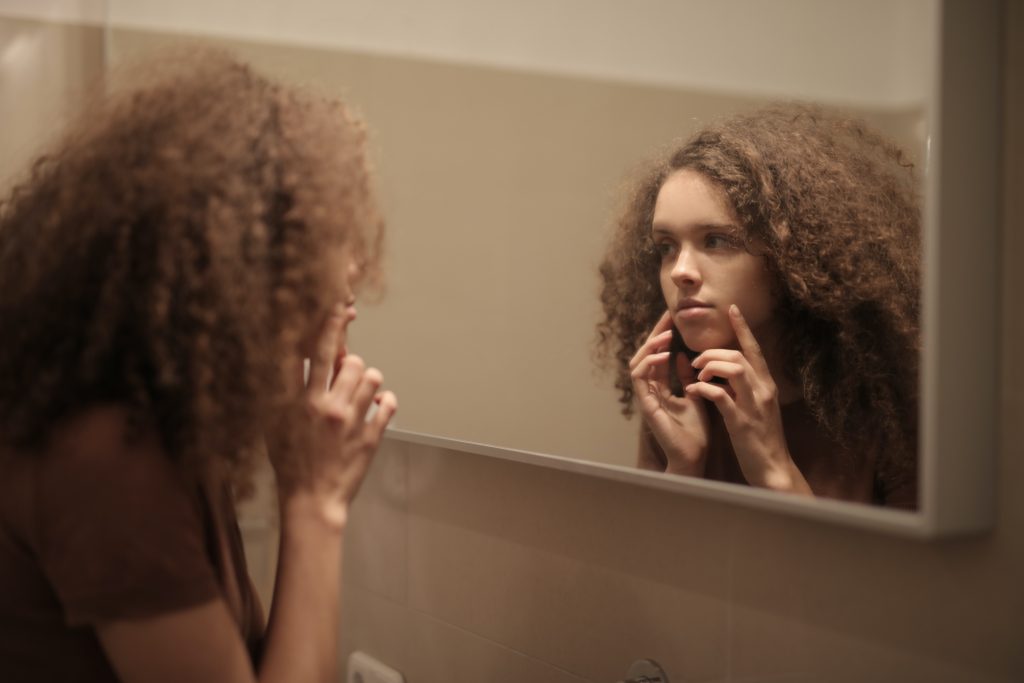 Woman looking in bathroom mirror and touching face with her fingers