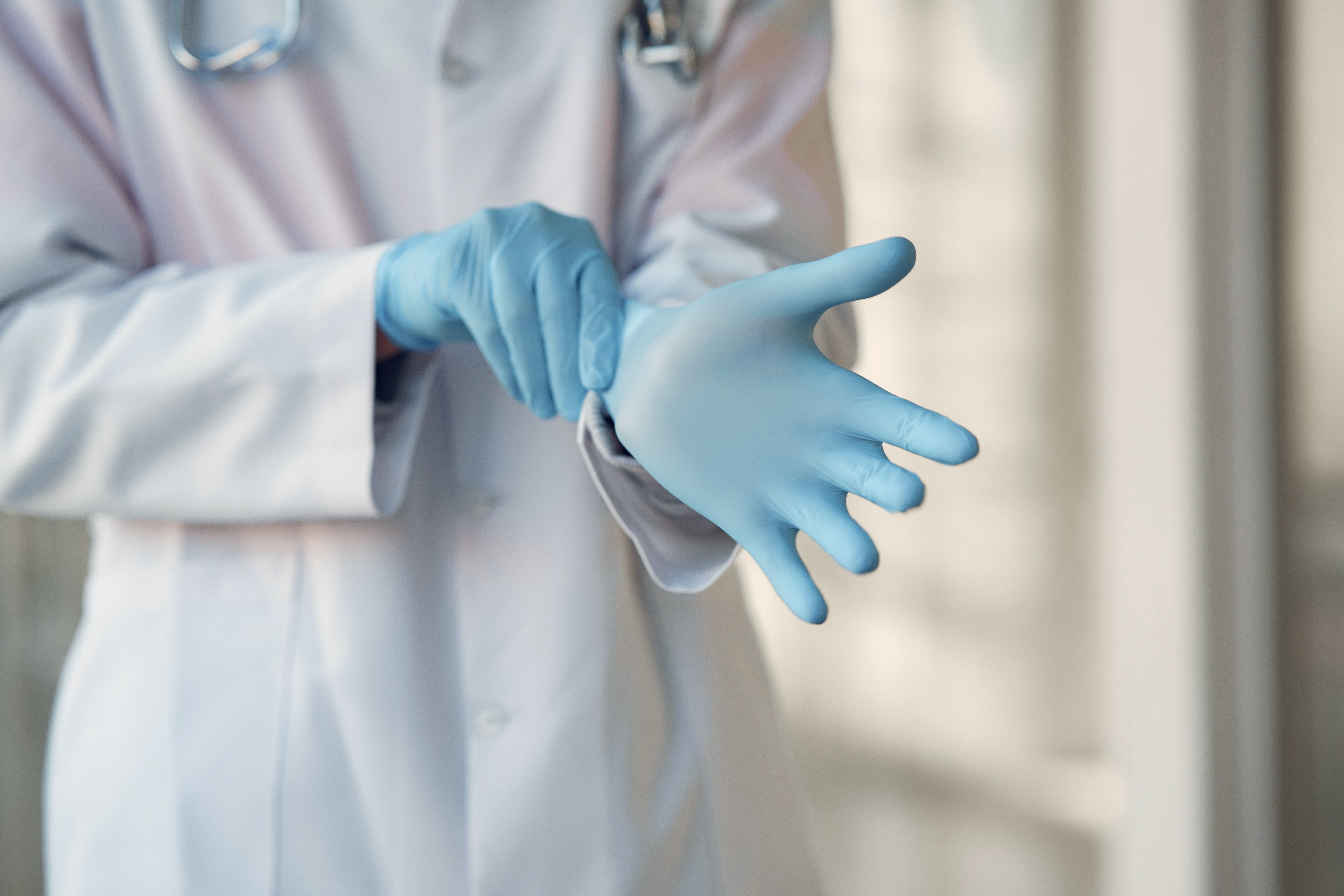 Doctor in white coat pulling on blue latex gloves