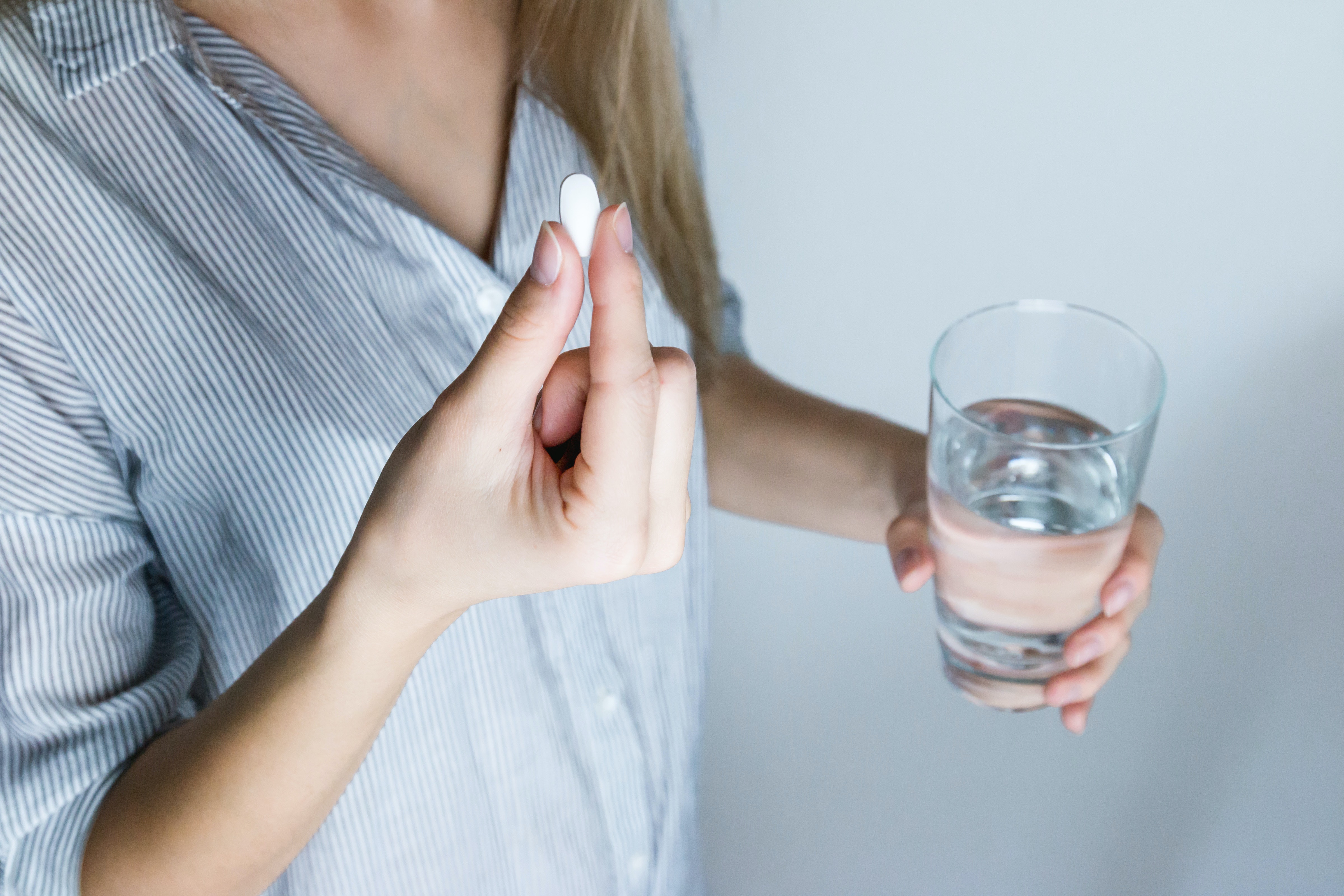 Woman in blue shirt holding white pill and glass of water