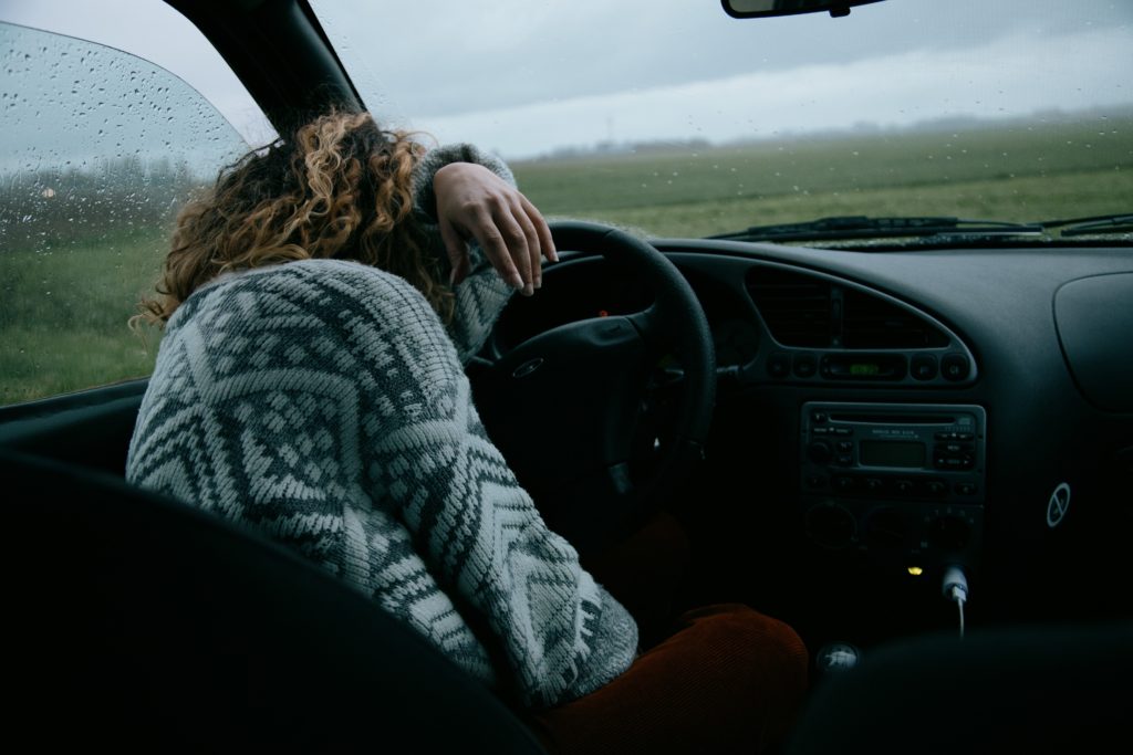 Woman sitting in parked car crying under gloomy sky