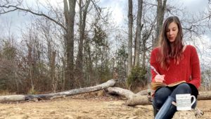 Jenna sitting in a log in the forest writing a blog post in a notebook