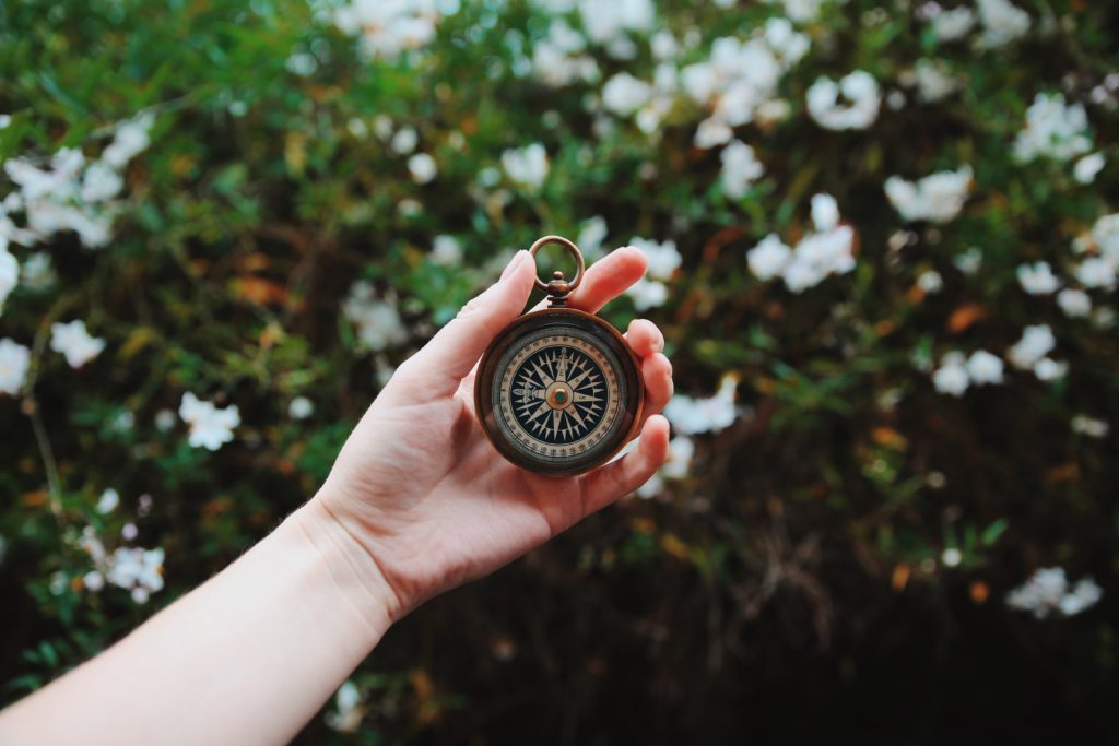Woman's hand holding compass in front of a flower bed