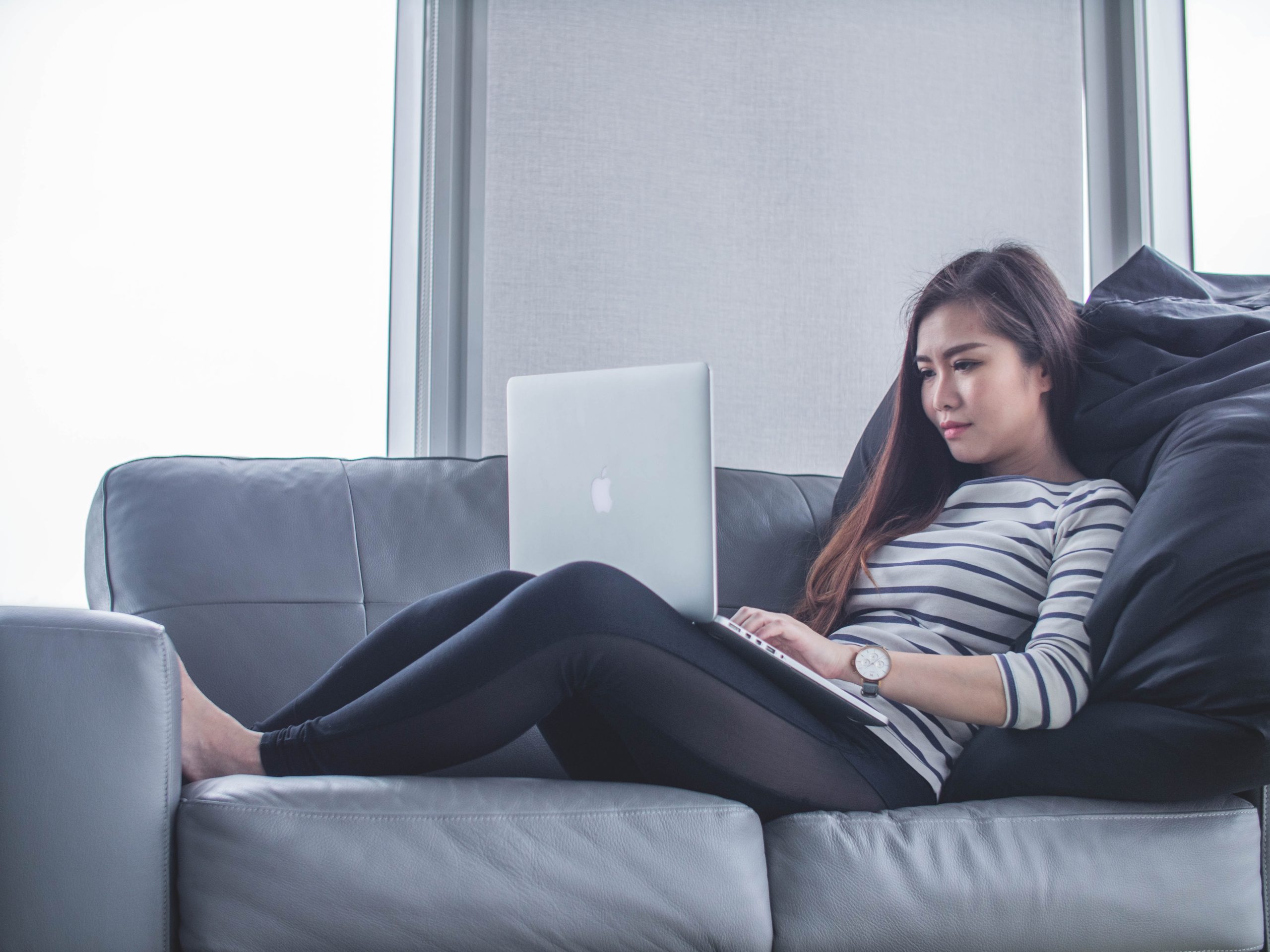 Woman laying on couch and reading PSC articles on laptop