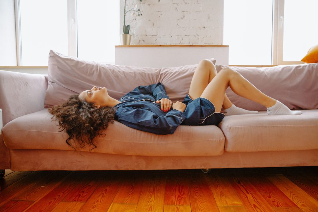 Woman in blue denim shirt and shorts clutching liver while laying on couch
