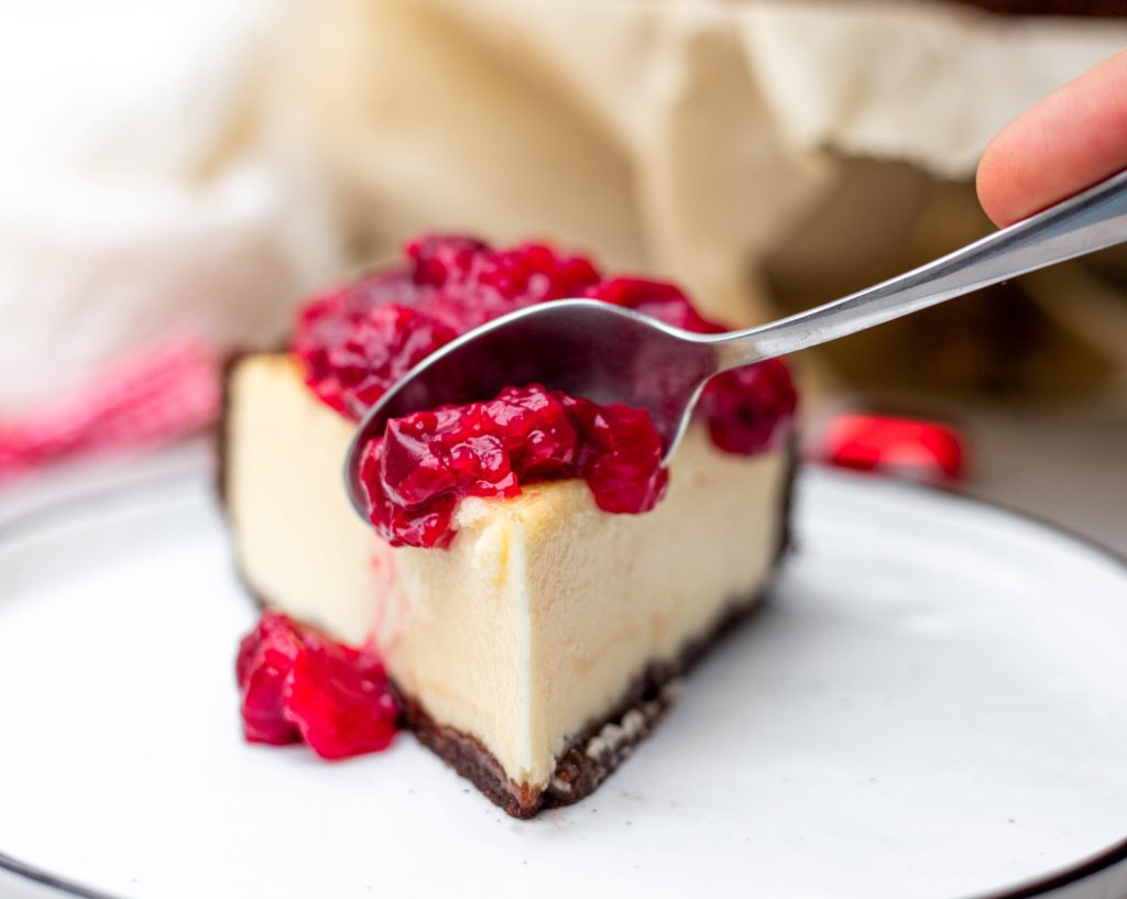 Person spooning slice of raspberry cheesecake