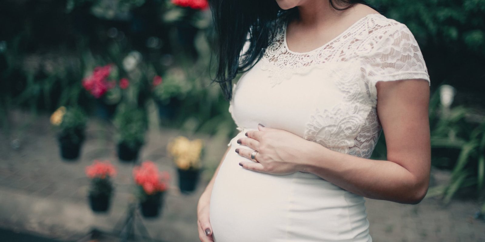 close up photo of pregnant woman in white dress holding her stomach