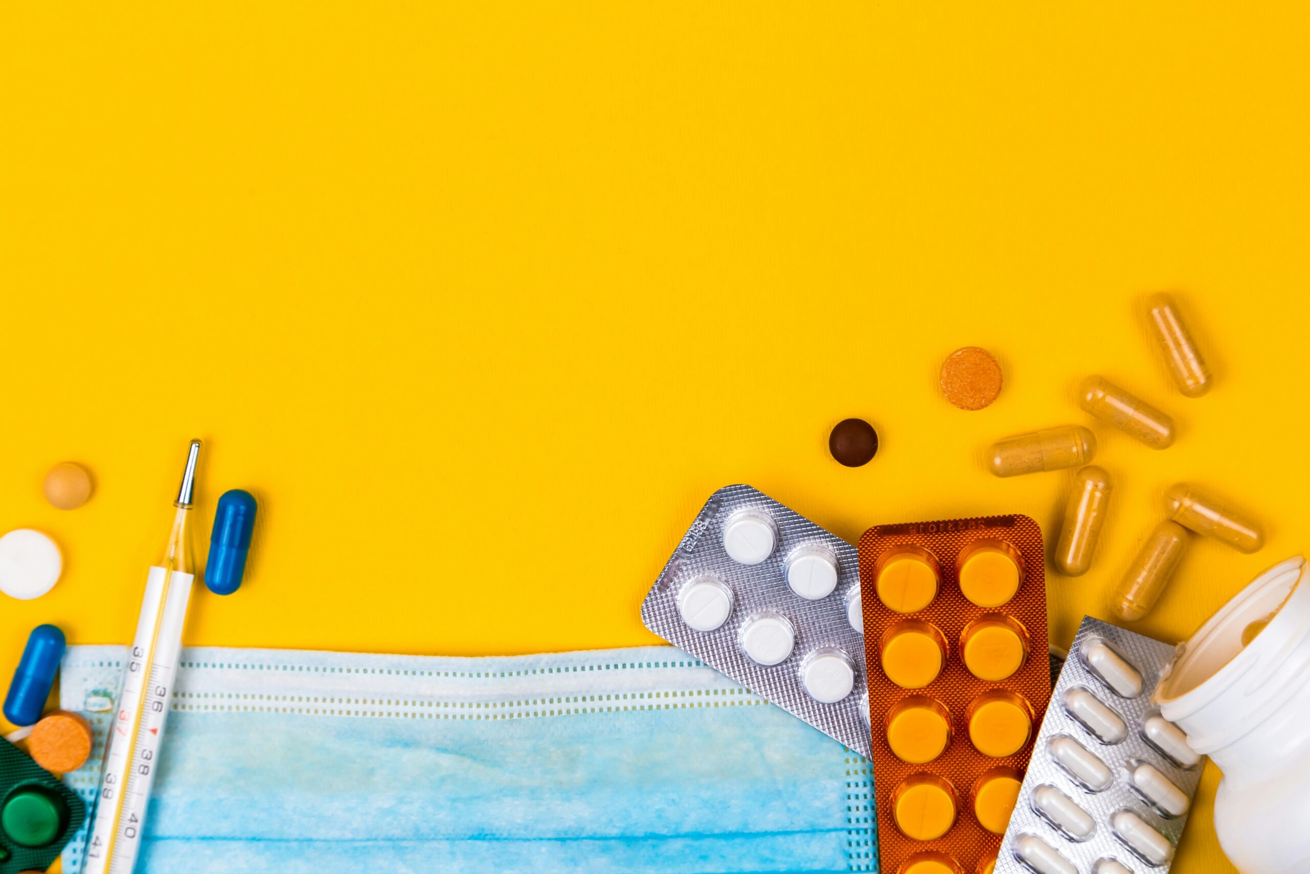 Orange background filled with different types of pills, a syringe, and a face mask