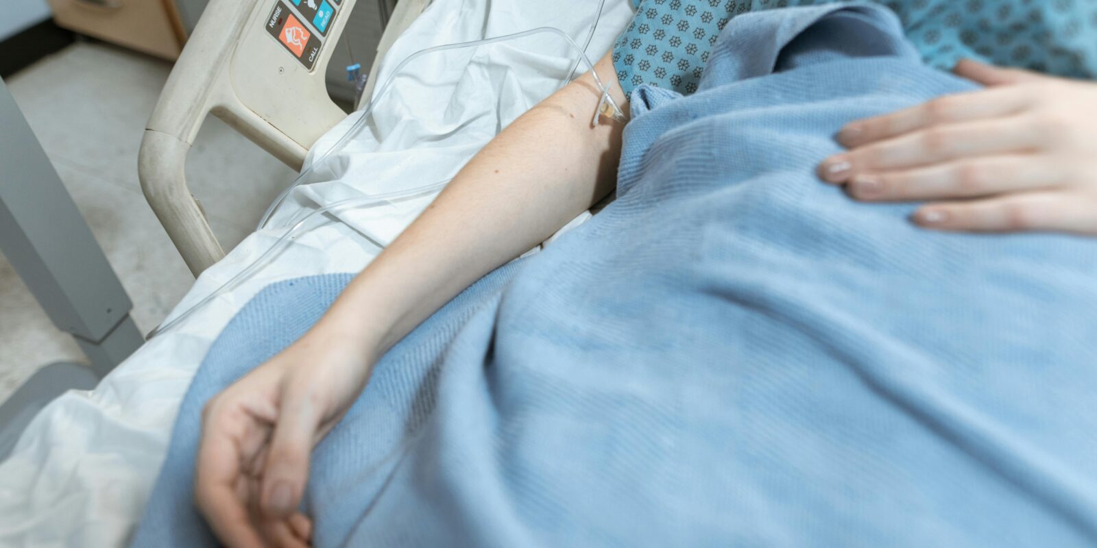 Woman in blue hospital gown and blanket laying in hospital bed with IV in arm and hand on her belly.