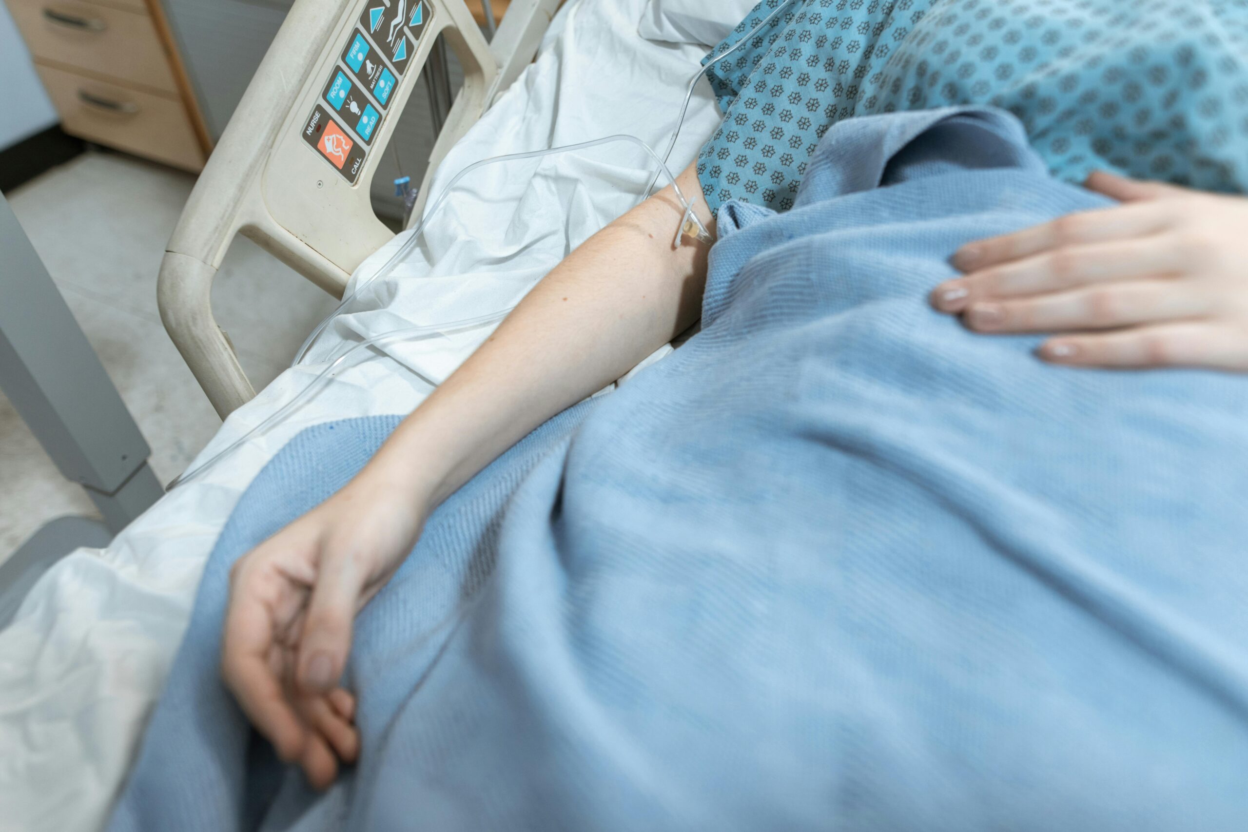 Woman in blue hospital gown and blanket laying in hospital bed with IV in arm and hand on her belly.