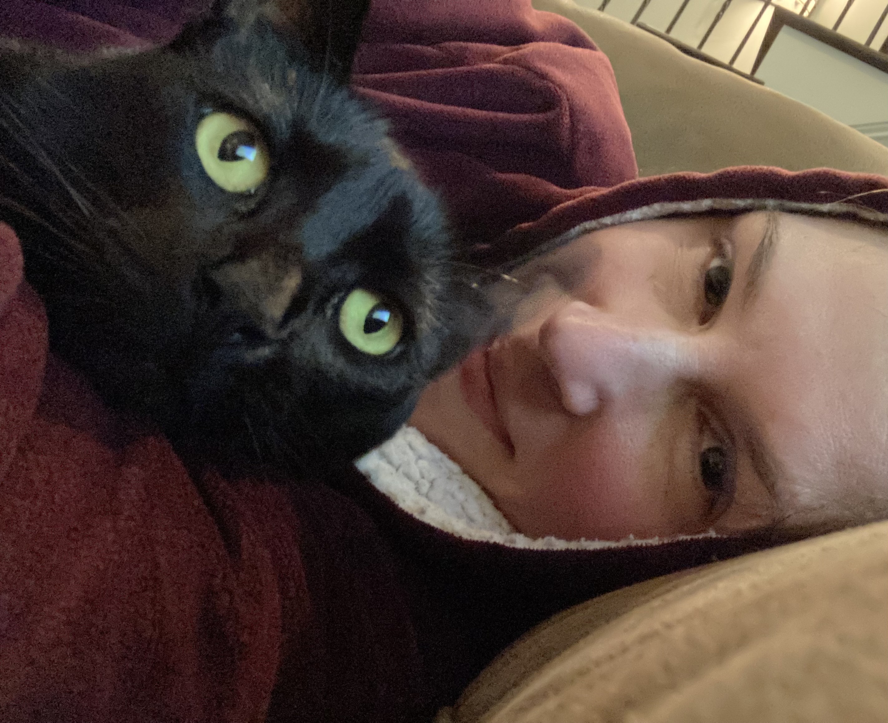 Jenna with large red sweatshirt and hood laying on couch with black cat Newbert