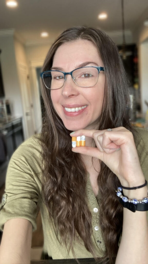 Jenna holding three white and orange Zenpep digestive enzyme capsules